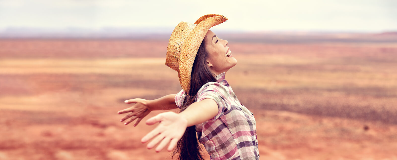 Shows a woman wearing a cowboy hair with her arms spread in happiness while smiling. Represents how freeing trauma counseling in Fort Worth, TX can be with a trauma therapist in Fort Worth, TX.