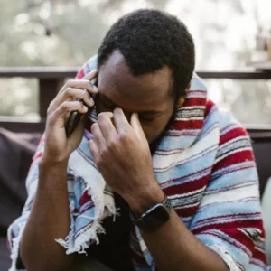 Shows a man on the phone holding the bridge of his nose in frustration. Represents how a fort worth trauma therapist and trauma therapy fort worth can help you identify how your trauma is impacting your relationships.