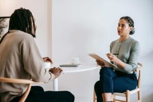 Shows a Fort Worth trauma therapist sitting at a table talking to a client. Represents how trauma therapy in fort worth, tx can help you heal your unprocessed trauma.