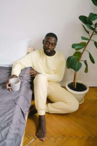 A man in yellow loungewear sits on the floor beside his bed, holding a cup, appearing deep in thought. Trauma counseling in Fort Worth can help individuals struggling with intimacy issues rooted in past trauma. A Fort Worth trauma therapist provides support to navigate emotional barriers and rebuild connection in relationships.